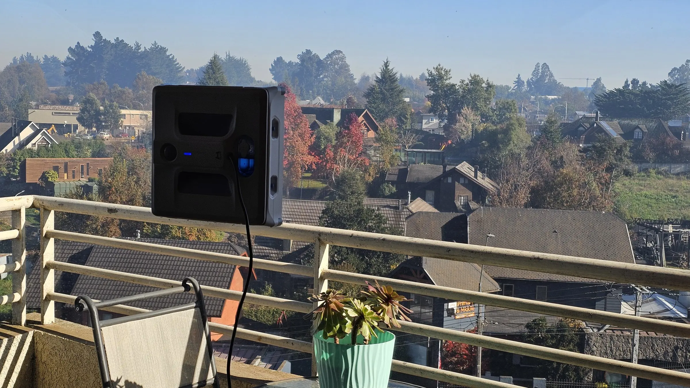 Robot limpiavidrios sobre un ventanal, con vista a un barrio residencial